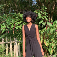 Ayooluwa smiling and standing in front of a fence and lush greenery.